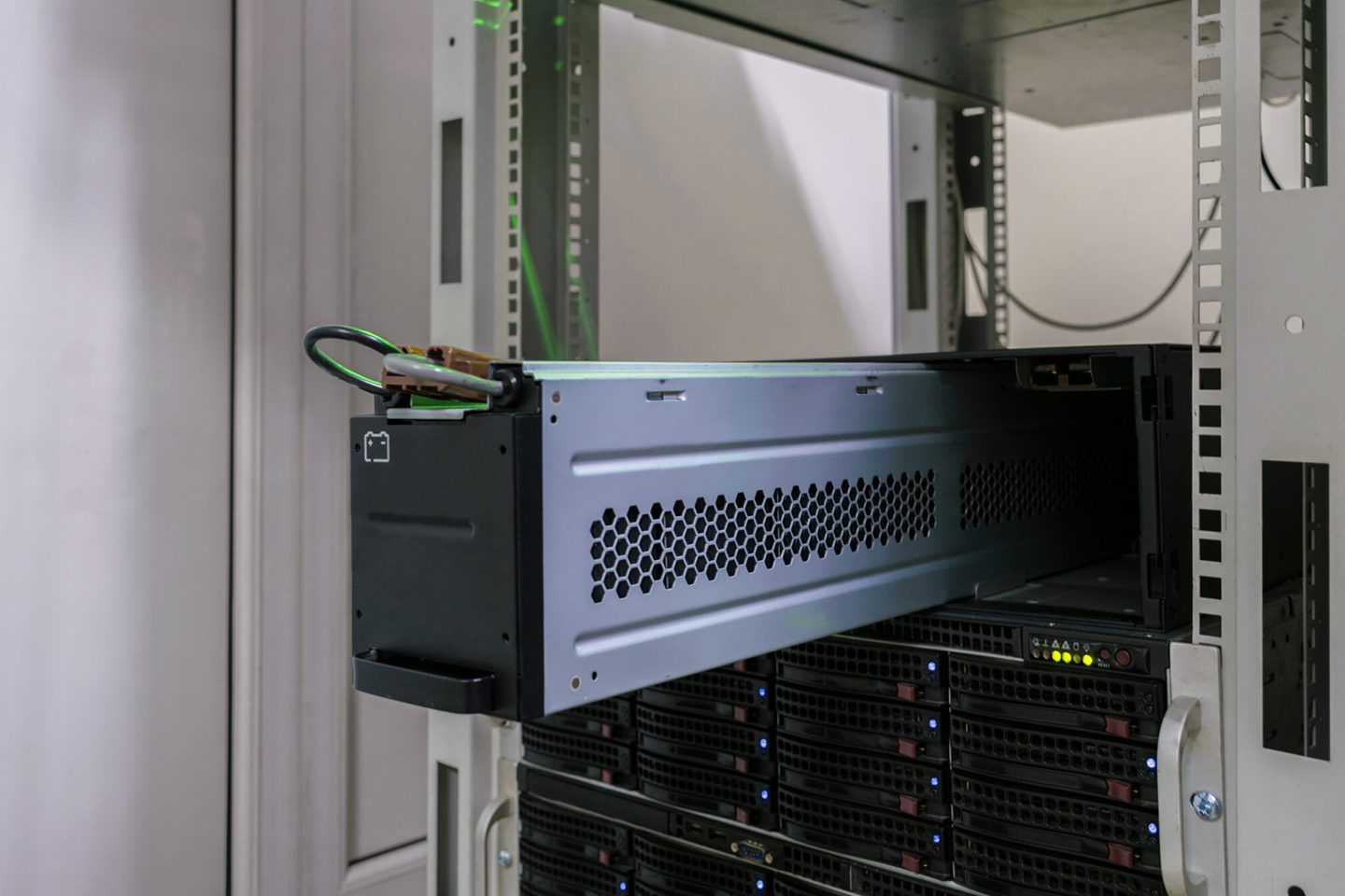 Server rack with a partially slid-out server drawer, displaying multiple cables and lights, in a data center environment.