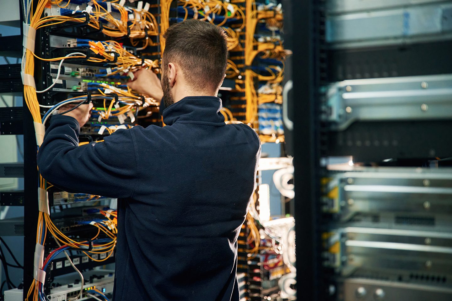 A person in a dark jacket is working on a complex network of cables in a server room, adjusting connections at a rack of equipment.