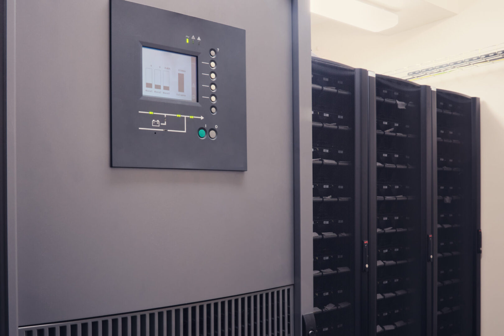 In the server room, the UPS battery is connected to an emergency power supply system A row of server racks is aligned in a brightly lit room, with a control panel displaying data on the front of one unit.