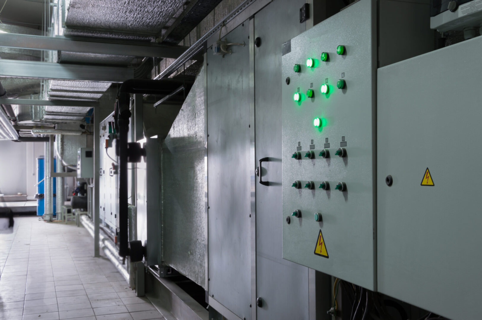 Two closed ventilation system control cubicles in the industrial ventilation room near to the ventilation unit Industrial control panel with green indicator lights and warning signs in a facility corridor.